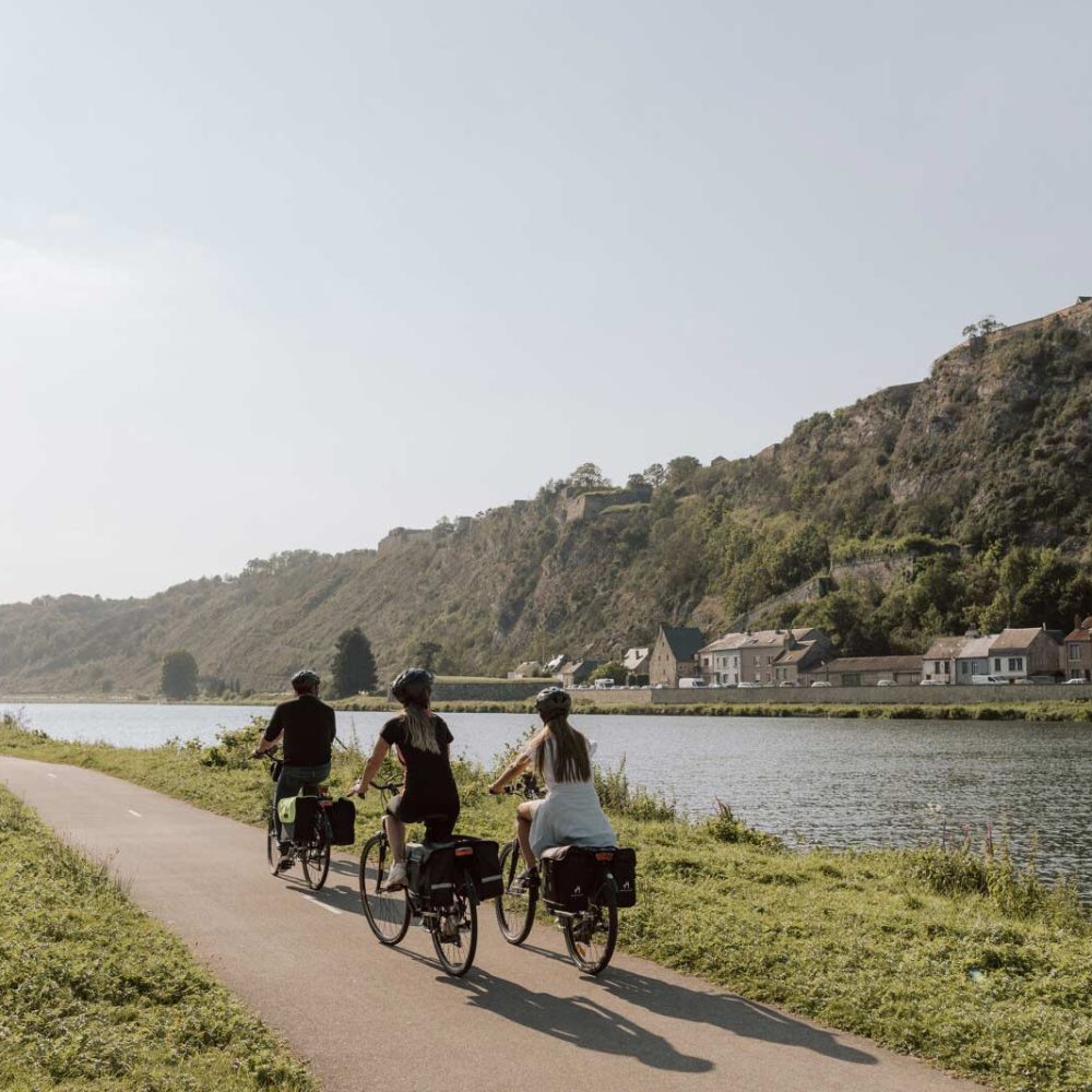 Cyclistes sur la voie verte Trans'Ardenne longeant la Meuse avec vue sur la citadelle de Charlemont, Parc naturel régional des Ardennes